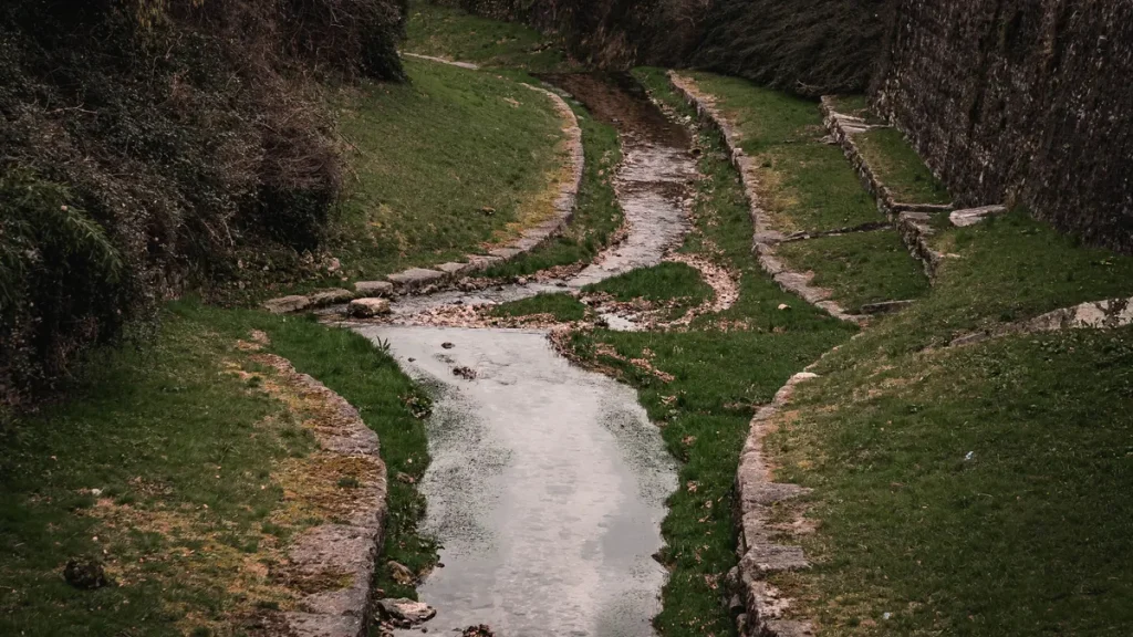 Shallow landscaped drainage channel carrying water through grass